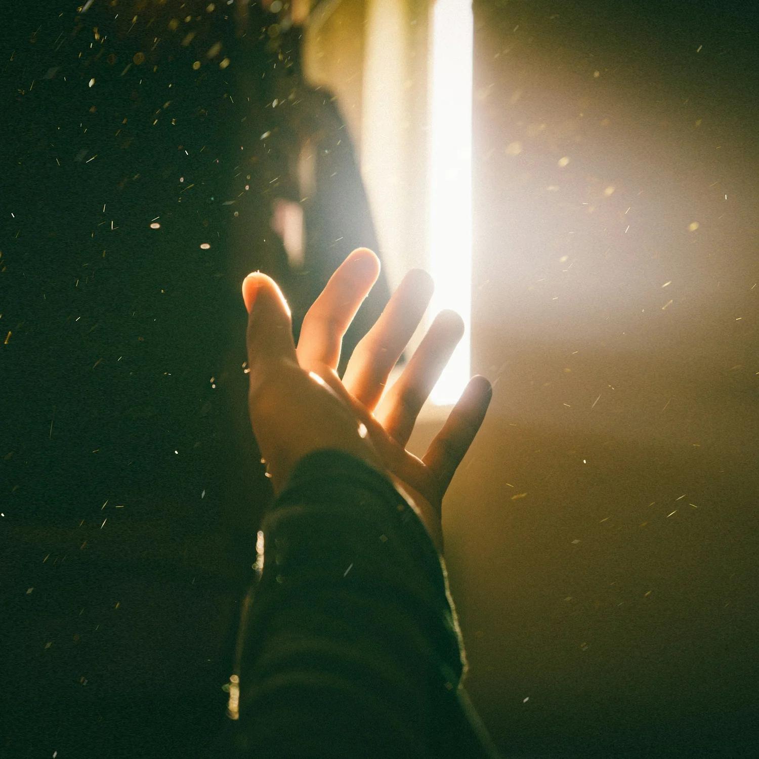 Une main tendue vers une lumière vive, avec des particules en suspension dans l'air.