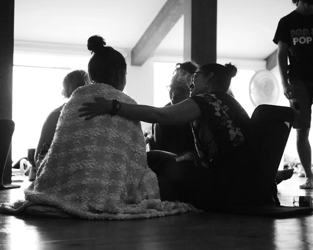 Groupe de personnes assises sur le sol, partageant un moment de complicité.